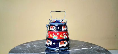 Colorful tiered hand painted Tiffin with animal designs placed on a marble surface against a beige wall.